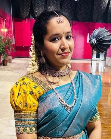 Woman wearing a blue saree, yellow embroidered blouse, traditional Indian jewelry, and jasmine flowers.