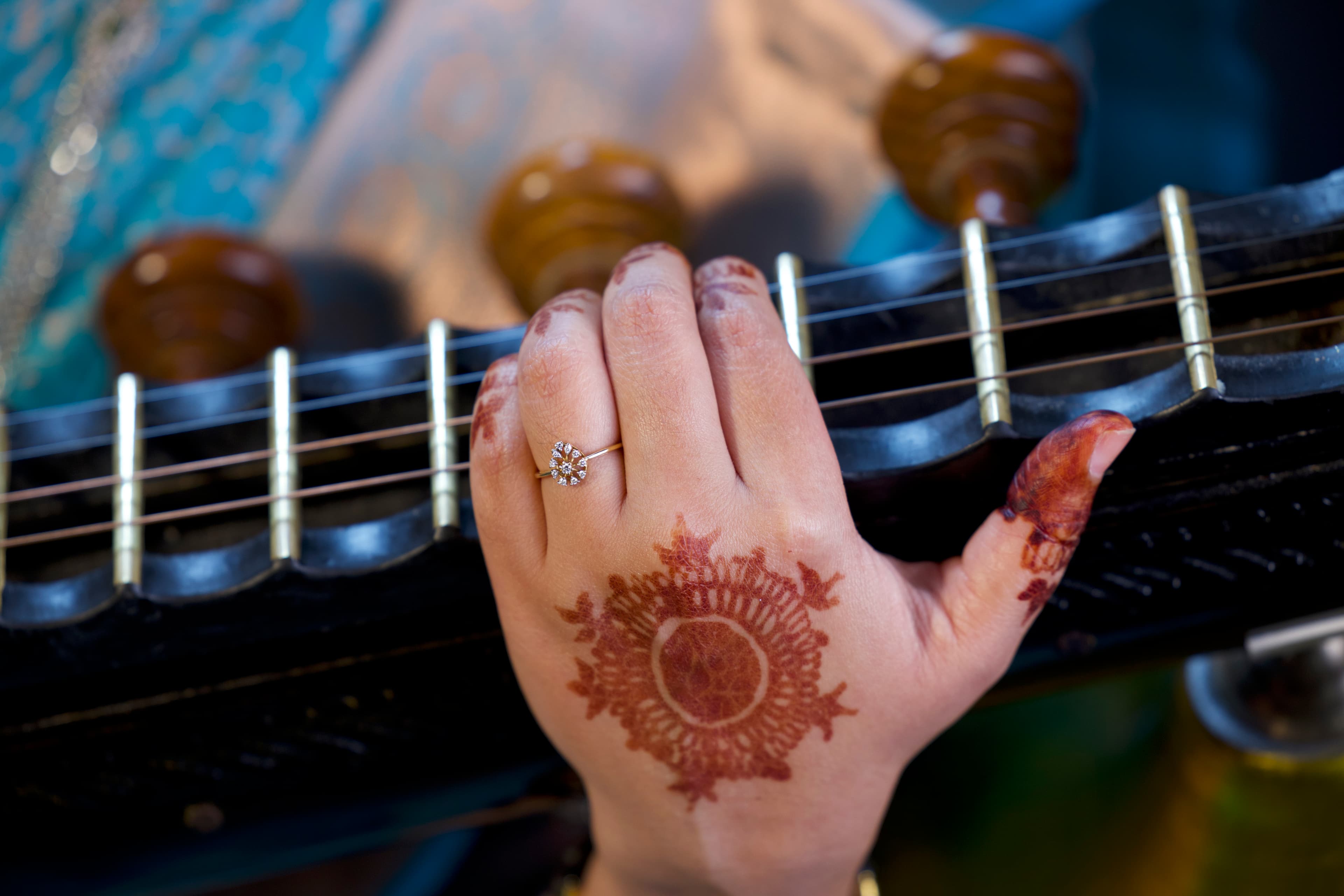 Hand with henna patterns and a gold ring resting on a traditional Indian veena.