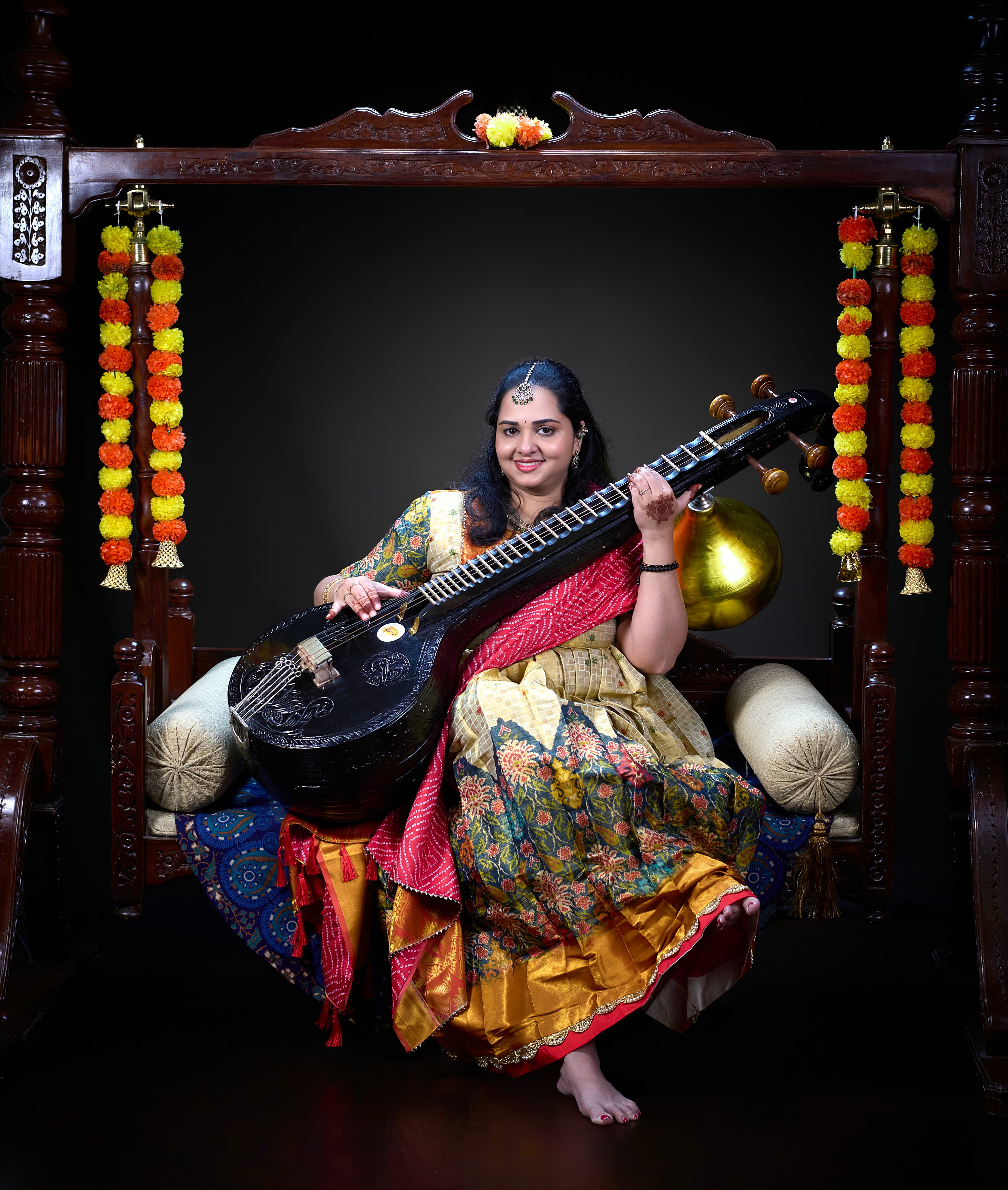 Woman in traditional saree holding a Saraswati Veena on a decorated wooden swing.